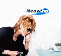 A Woman Talking On A Phone In Front Of A Neonwing Sign GIF