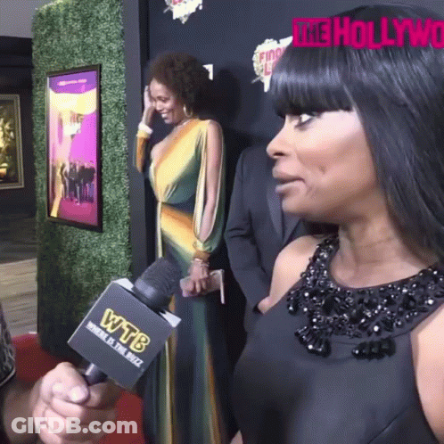 A Woman Talks Into A Wtb Microphone While Standing On A Red Carpet GIF