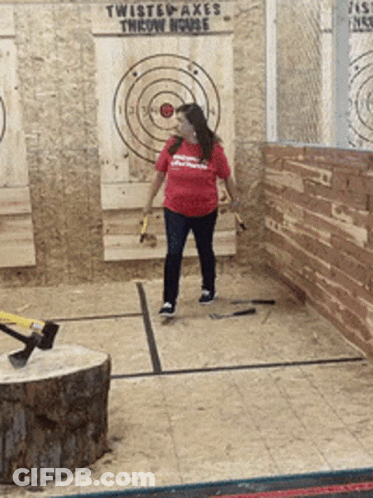 A Woman Throws An Axe In Front Of A Twisted Axes Throw House Sign GIF