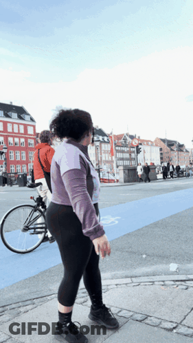 A Woman Walking Across A Street With A Bicycle Behind Her GIF