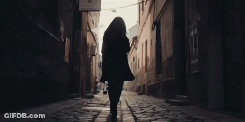 A Woman Walking Down A Cobblestone Street With A Sign That Says ' A Few Steps ' On It GIF