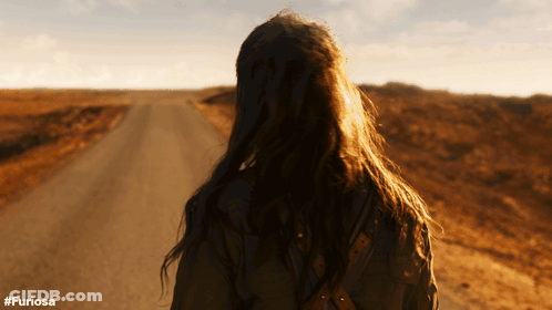 A Woman Walking Down A Dirt Road With The Hashtag #Furiosa On The Bottom GIF