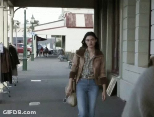 A Woman Walking Down A Sidewalk In Front Of A Store That Says ' A & A ' On It GIF
