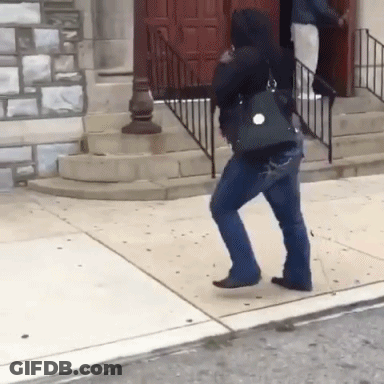 A Woman Walking Down A Sidewalk With A Purse On Her Back GIF