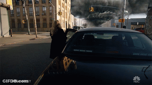 A Woman Walking Down A Street Next To A Car That Says Nbc On It GIF