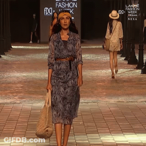 A Woman Walks Down A Runway At A Fashion Show GIF