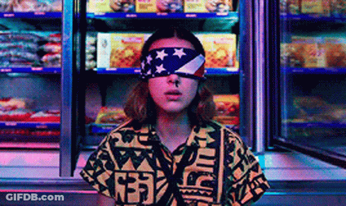 A Woman Wearing A Bandana With An American Flag On Her Eyes Is Standing In Front Of A Refrigerator . GIF
