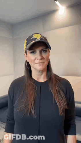 A Woman Wearing A Baseball Cap And A Black Shirt Is Making A Face . GIF