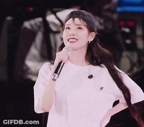 A Woman Wearing A Baseball Cap And A White Shirt Is Holding A Microphone And Smiling GIF