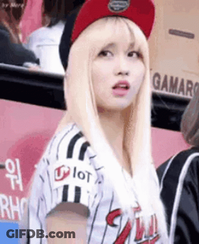 A Woman Wearing A Baseball Uniform And A Red Hat Is Standing In A Crowd . GIF