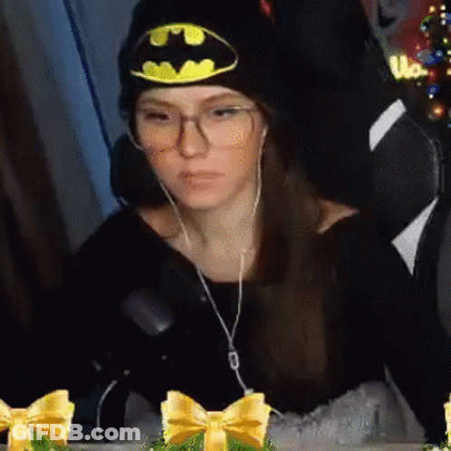 A Woman Wearing A Batman Hat And Glasses Is Sitting In A Chair With Headphones On . GIF