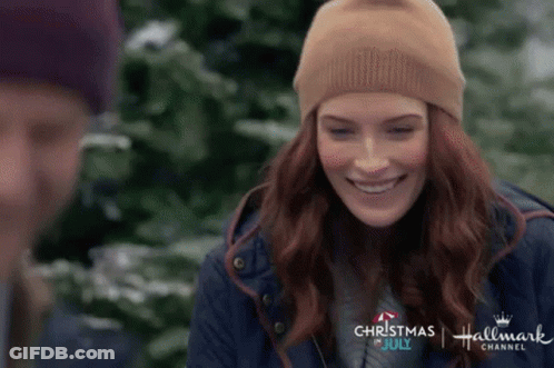 A Woman Wearing A Beanie Is Smiling In Front Of A Man In A Blue Jacket . GIF