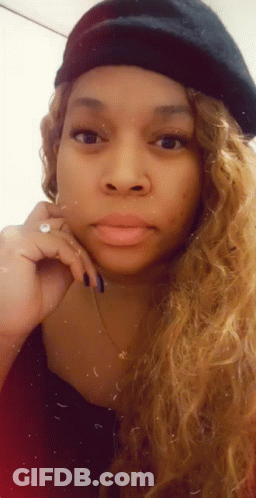 A Woman Wearing A Beret And A Necklace Is Looking At The Camera . GIF