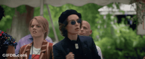 A Woman Wearing A Beret And Sunglasses Stands In A Crowd GIF