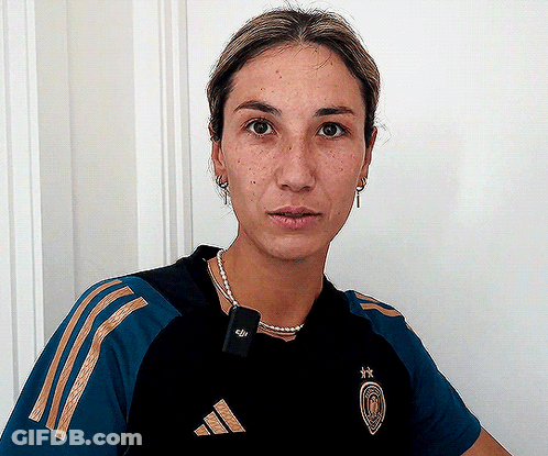 A Woman Wearing A Black And Gold Adidas Shirt Looks At The Camera GIF
