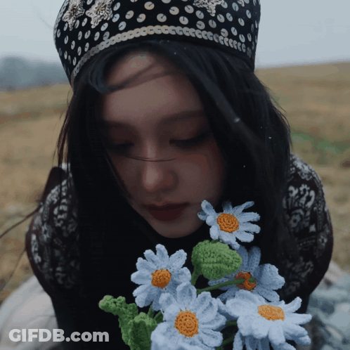 A Woman Wearing A Black And White Polka Dot Hat Holds A Bouquet Of Crocheted Daisies GIF
