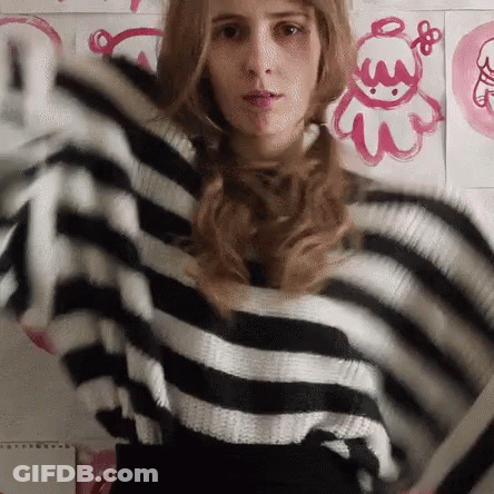 A Woman Wearing A Black And White Striped Sweater Is Standing In Front Of A Wall With Pink Drawings On It GIF