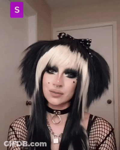 A Woman Wearing A Black And White Wig And A Choker With The Letter S On The Bottom GIF
