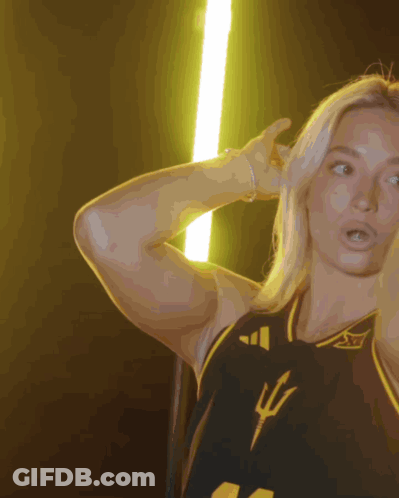 A Woman Wearing A Black And Yellow Jersey With A Trident On The Front GIF
