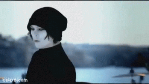 A Woman Wearing A Black Beanie And A Black Turtleneck Is Standing In Front Of A Body Of Water . GIF