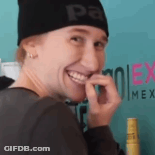 A Woman Wearing A Black Beanie Is Smiling And Biting Her Finger . GIF
