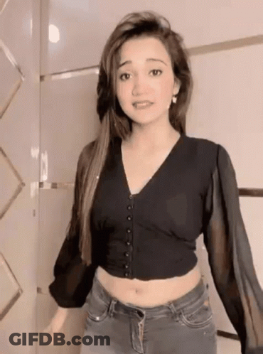 A Woman Wearing A Black Crop Top And Jeans Is Standing In Front Of A Wall . GIF