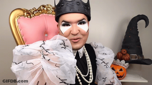 A Woman Wearing A Black Crown And Pearls Is Sitting In A Pink Chair GIF