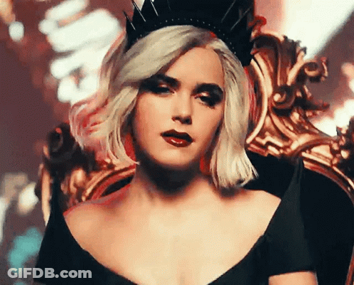 A Woman Wearing A Black Dress And A Crown Is Sitting In A Chair . GIF