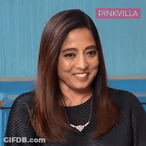 A Woman Wearing A Black Dress And A Necklace Is Smiling In Front Of A Pinkvilla Banner GIF