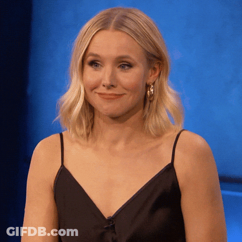 A Woman Wearing A Black Dress And Hoop Earrings Smiles GIF