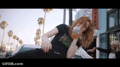 A Woman Wearing A Black Gucci T-Shirt Drinks From A Glass GIF