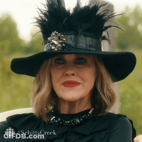A Woman Wearing A Black Hat And A Black Shirt With #Schitts Creek Written On The Bottom GIF