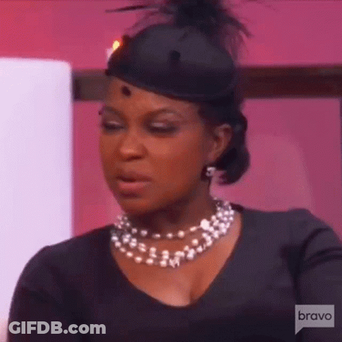 A Woman Wearing A Black Hat And A Pearl Necklace . GIF