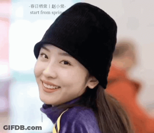 A Woman Wearing A Black Hat And A Purple Sweater Smiles For The Camera GIF