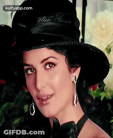 A Woman Wearing A Black Hat And Earrings Is Smiling For The Camera . GIF