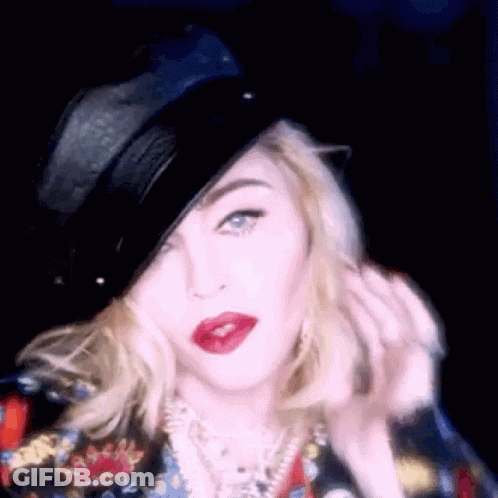 A Woman Wearing A Black Hat And Red Lipstick Is Looking At The Camera . GIF