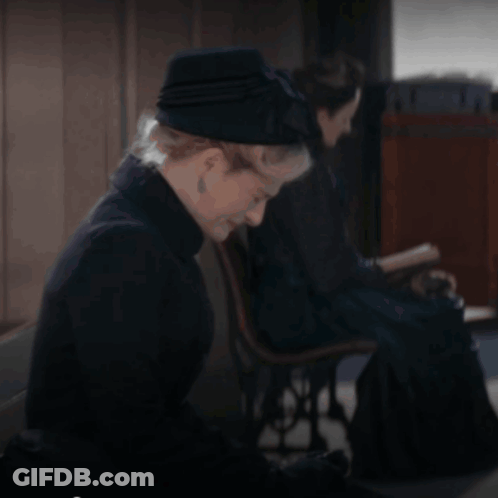 A Woman Wearing A Black Hat Sits In A Chair GIF