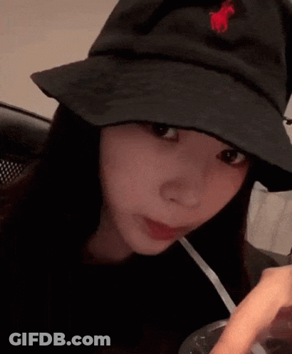 A Woman Wearing A Black Hat With A Red Horse On It Is Drinking Through A Straw . GIF