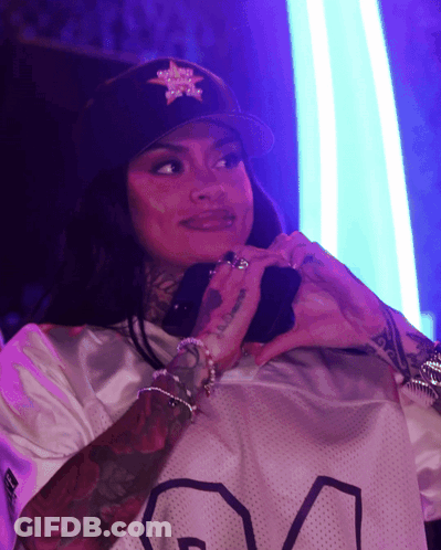 A Woman Wearing A Black Hat With A Star On It Is Making A Heart Shape With Her Hands GIF