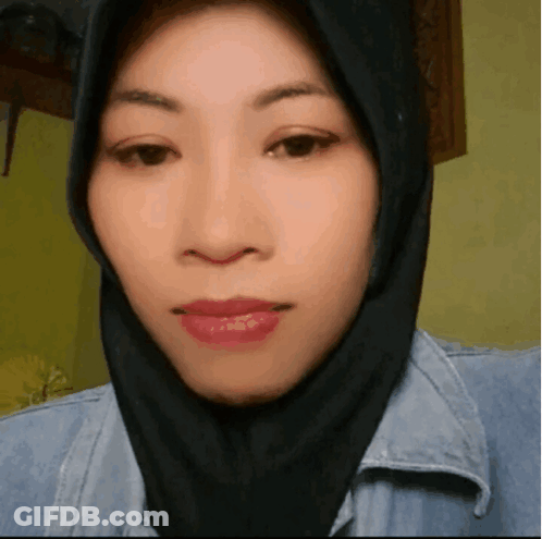 A Woman Wearing A Black Hijab And A Denim Jacket Looks At The Camera GIF