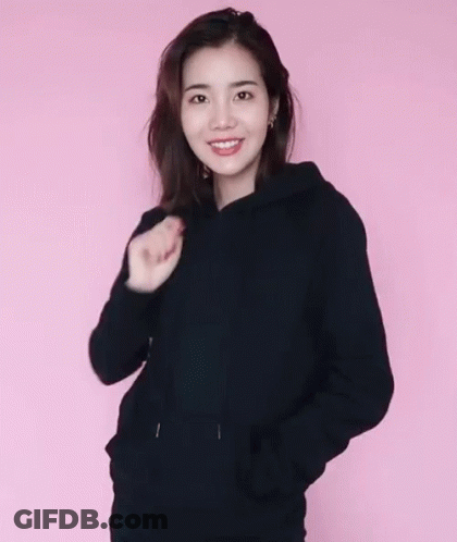 A Woman Wearing A Black Hoodie And A Black Hat Against A Pink Background GIF