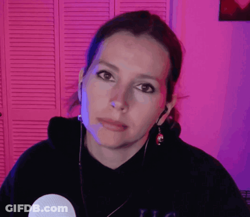 A Woman Wearing A Black Hoodie And Earbuds Looks At The Camera With A Serious Look On Her Face GIF