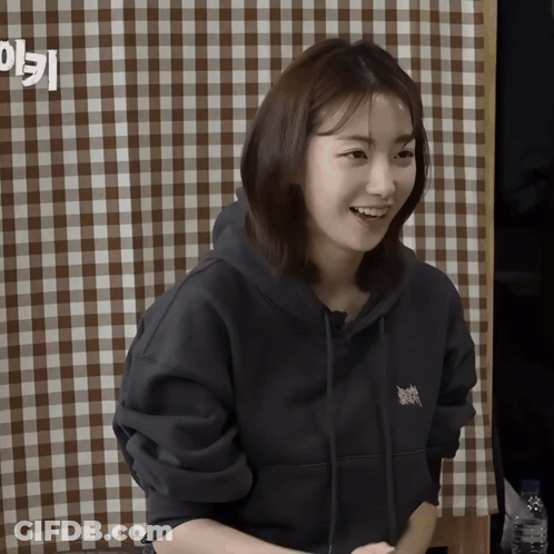 A Woman Wearing A Black Hoodie Smiles In Front Of A Checkered Tablecloth GIF