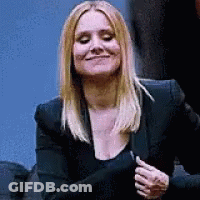 A Woman Wearing A Black Jacket And A Black Top Is Smiling And Looking At The Camera . GIF