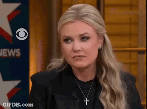 A Woman Wearing A Black Jacket And A Cross Necklace Is Sitting In Front Of A News Sign . GIF