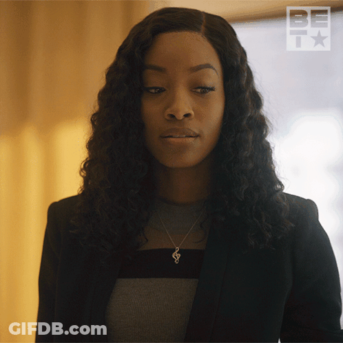 A Woman Wearing A Black Jacket And A Necklace With A S On It GIF