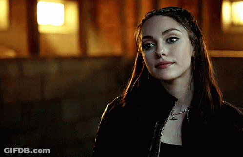 A Woman Wearing A Black Jacket And A Necklace With The Letter T On It GIF