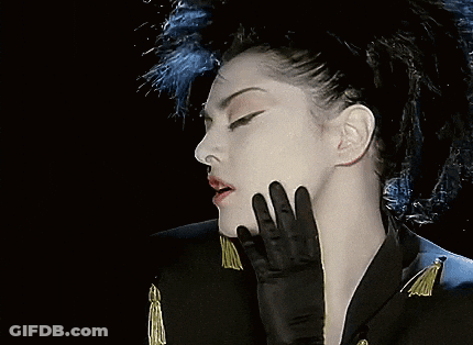 A Woman Wearing A Black Jacket Has Red Beads Hanging From Her Ears GIF