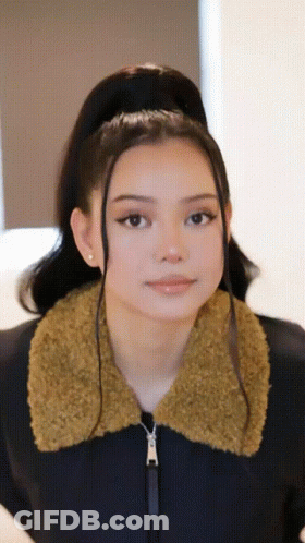 A Woman Wearing A Black Jacket With A Furry Collar Looks At The Camera GIF