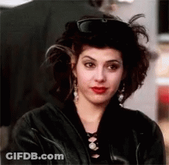 A Woman Wearing A Black Leather Jacket And A Hat Is Looking At The Camera . GIF